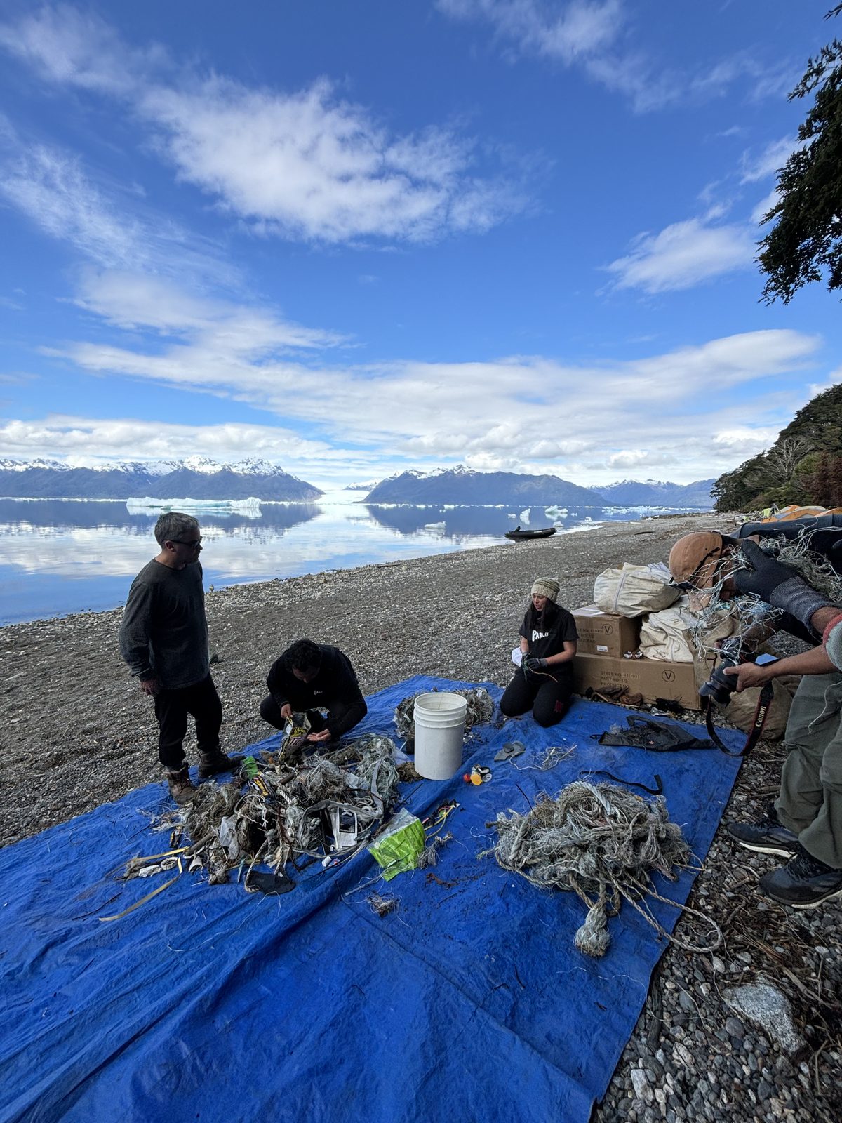 Voluntarios separando residuos en la playa, con el lago y las montañas al fondo